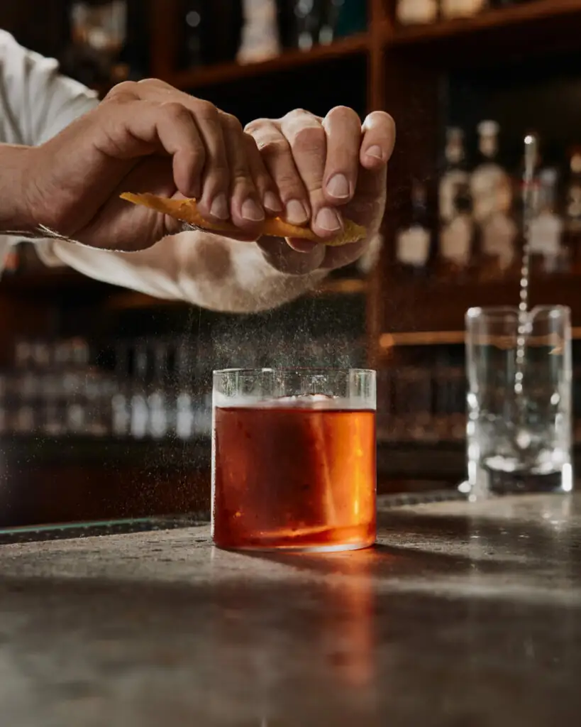 A bartender squeezing an orange peel over a cocktail during preparation in Mission Pacific Hotel