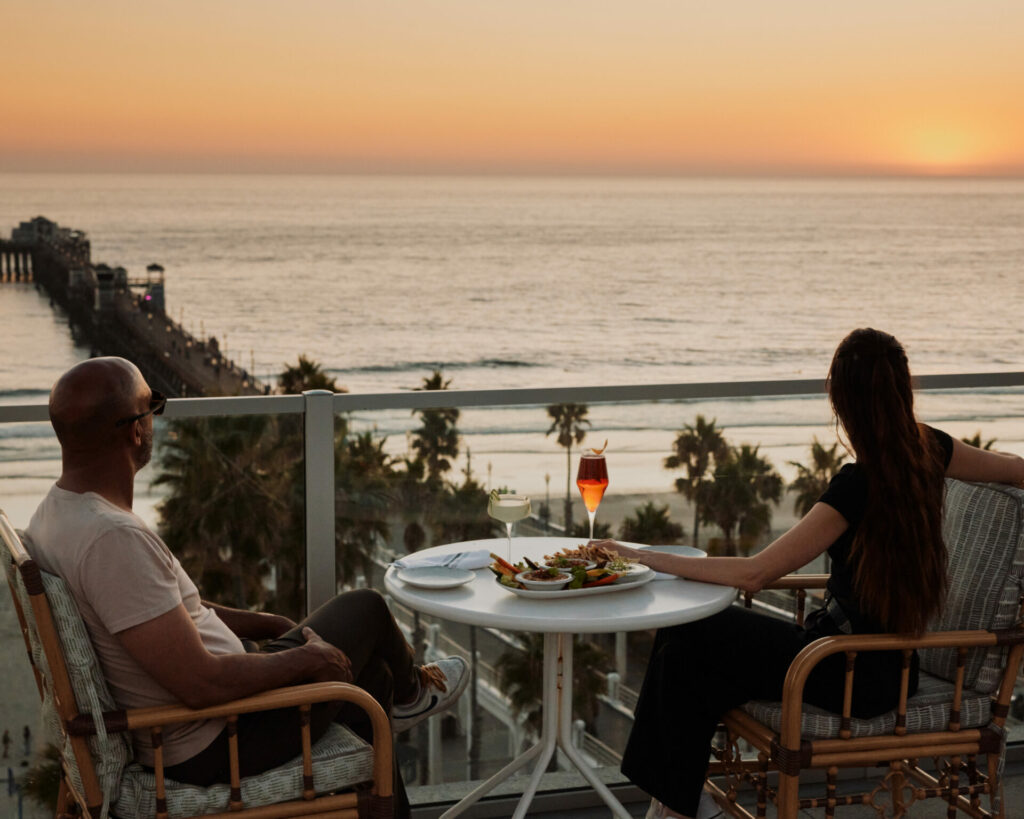 A couple dining on the terrace overlooking the sea and pier at sunset