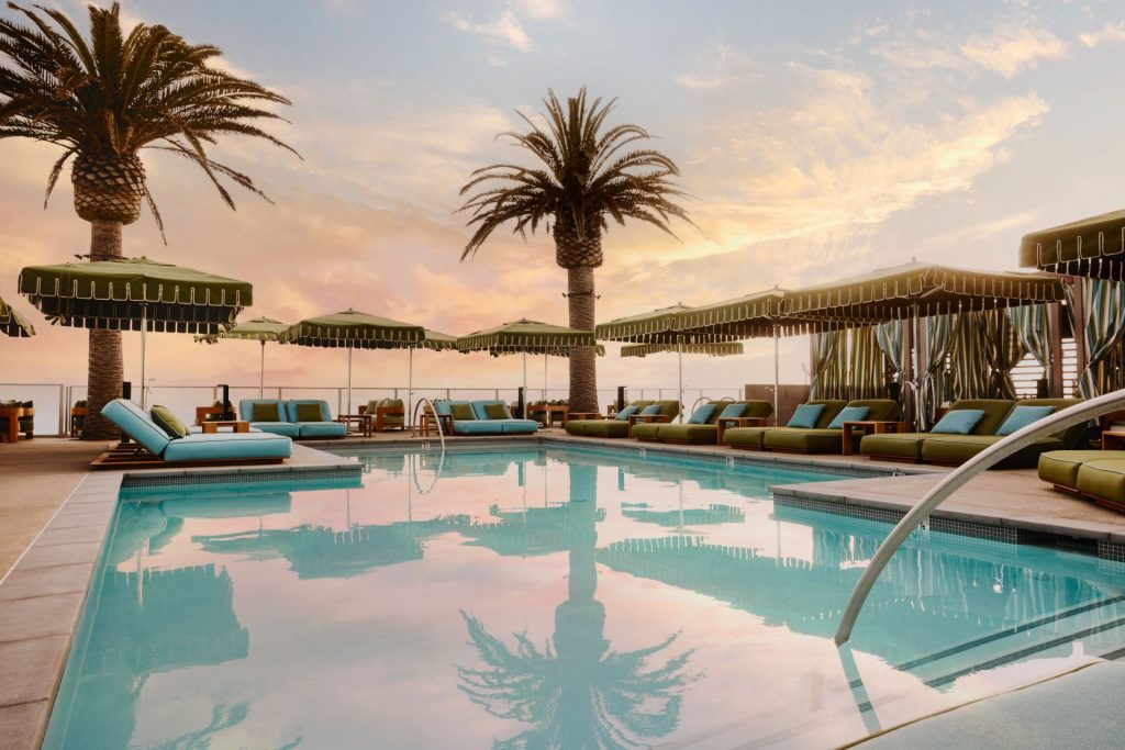 Hotel pool on a rooftop featuring daybeds, umbrellas, and palm trees