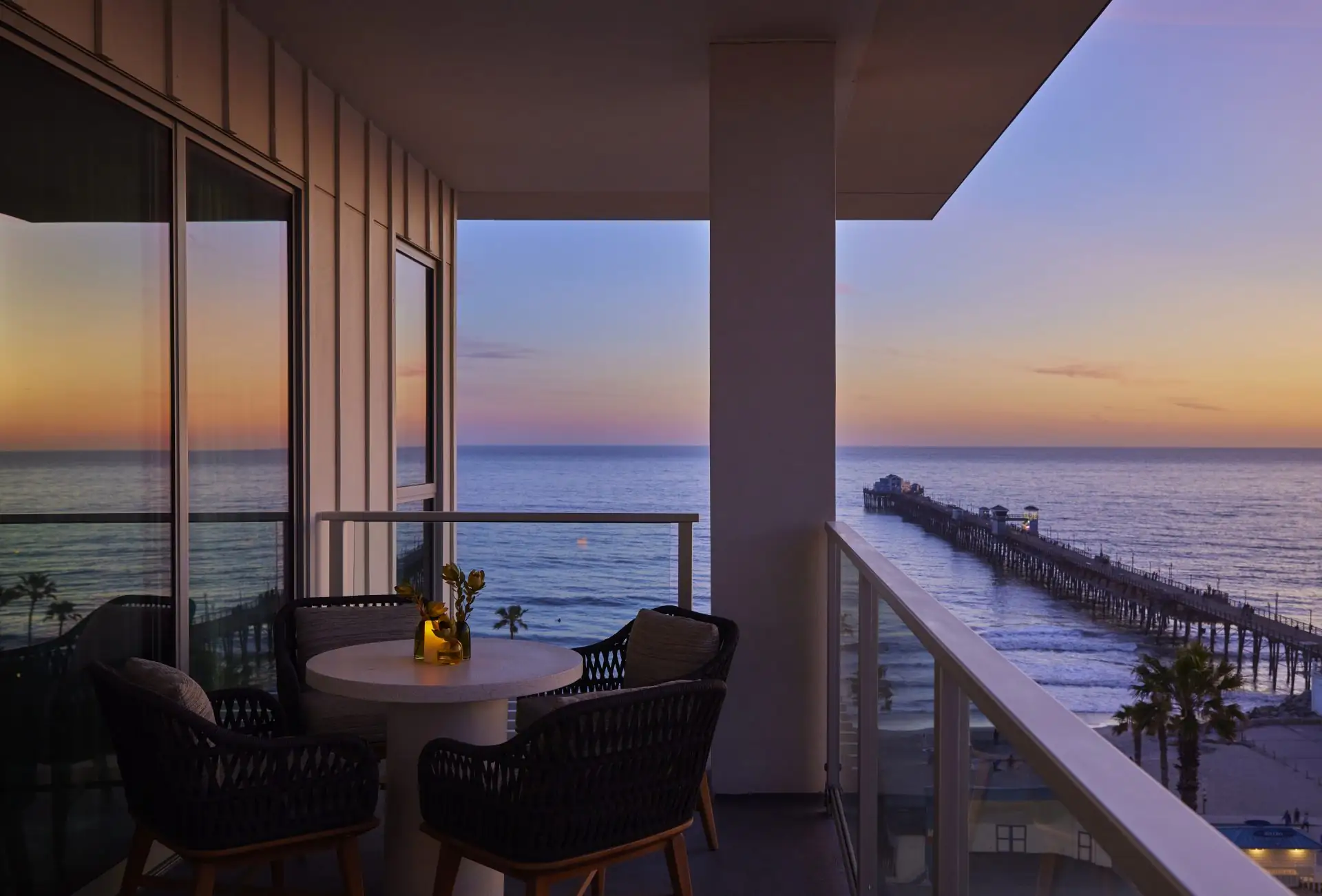 Private balcony with ocean and pier views at sunset, featuring cozy seating and ambient lighting
