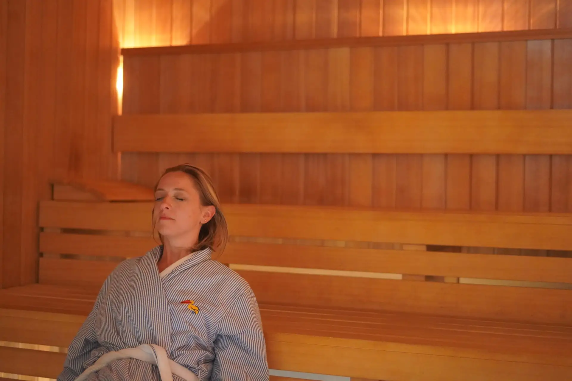 Guest relaxing in wooden sauna at mission pacific beach resort, wearing striped robe under warm, soothing ambient light.