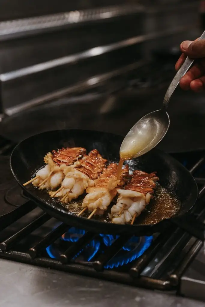 Seafood skewers sizzling in a pan as sauce is spooned over them at Valle restaurant’s kitchen.
