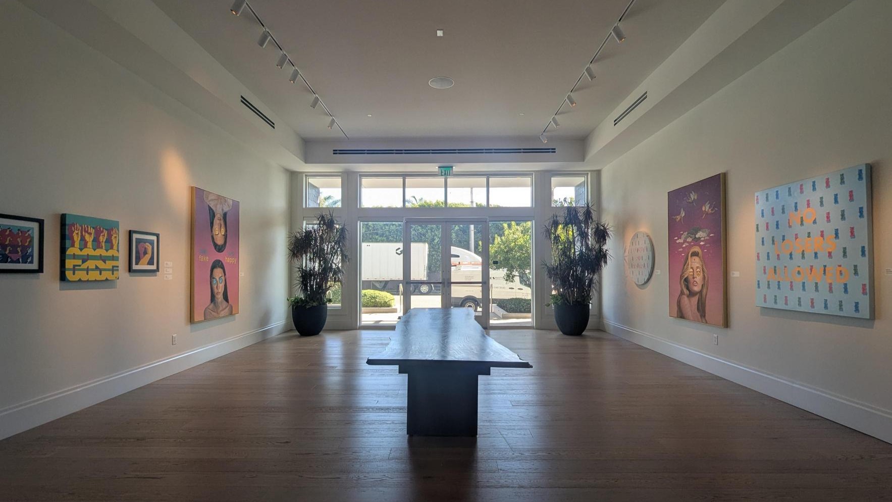 Modern art gallery with a central bench, potted plants, and colorful contemporary artworks on the walls