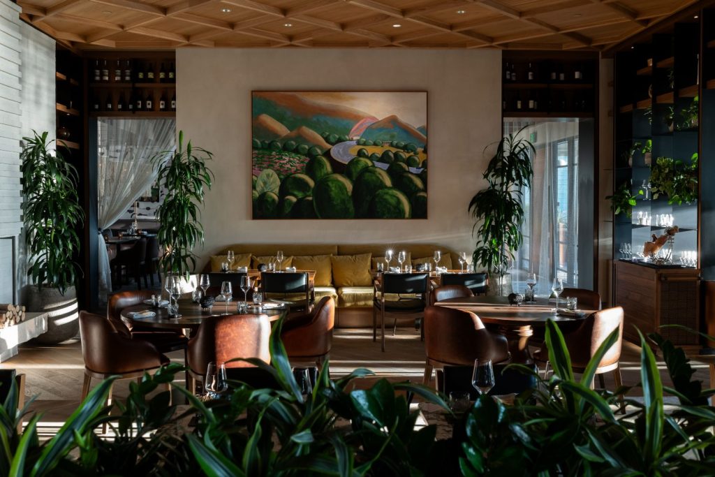 Elegant restaurant dining room with warm wood ceilings, leather seating, plants, and softly lit tables.