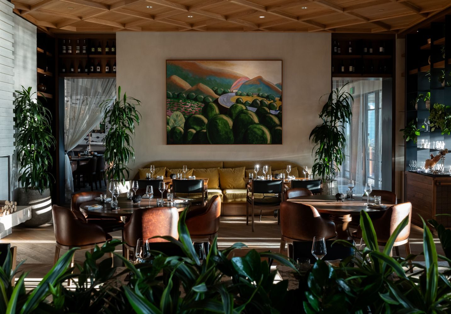 Elegant restaurant dining room with warm wood ceilings, leather seating, plants, and softly lit tables.