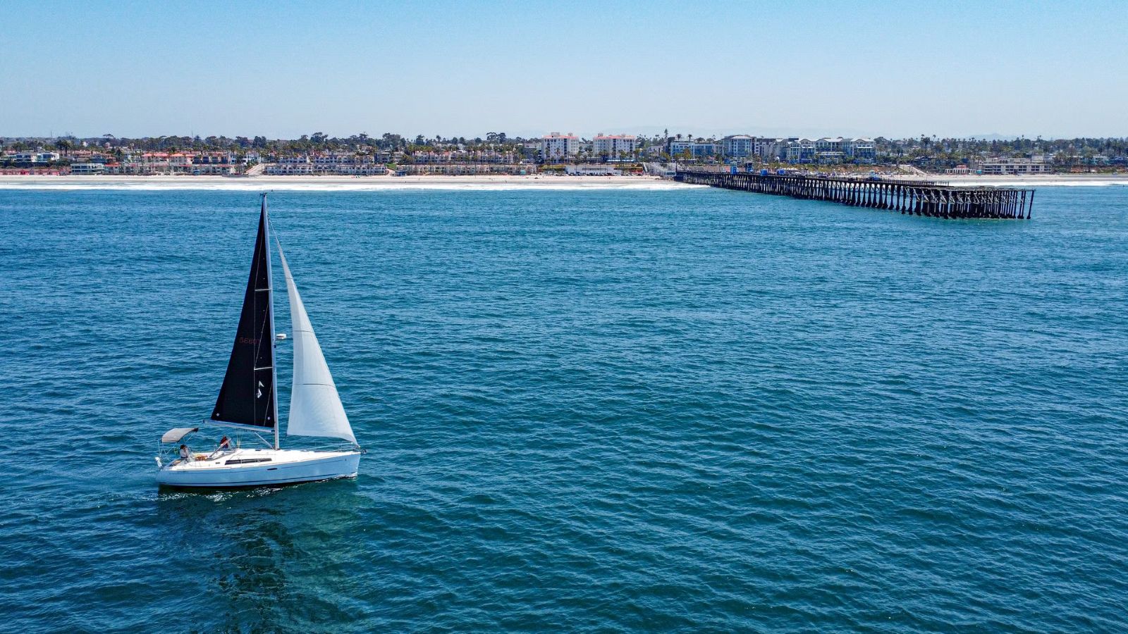 Sailboat off oceanside pier with mission pacific and the coastline in the background